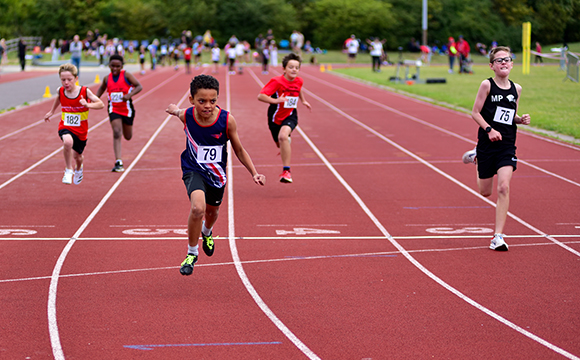 a number of children running a middle distance track with the SSAthletics' athlete frontrunning 