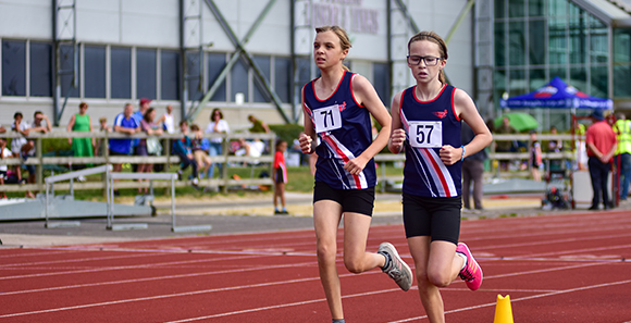 two girls running middle distance on a racetrack 
