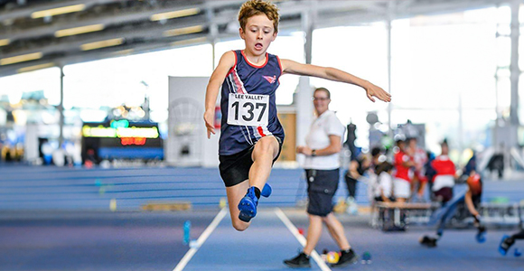 a child performing a long jump down a track indoors