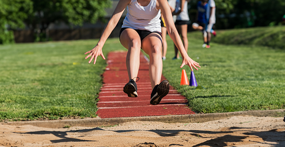 a person in the middle of doing a triple jump into a sand pit