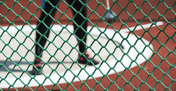 a person holding a hammer in preparation for a hammer throw with a green mesh fence in front of them