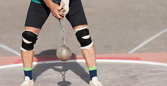 a person with bent legs holding a hammer in preparation for a hammer throw